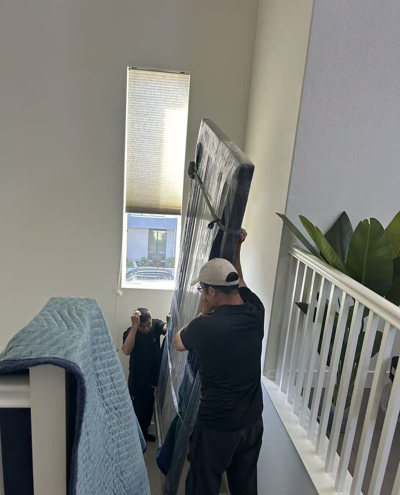 Hello Movers crew carrying a wrapped piece up a staircase