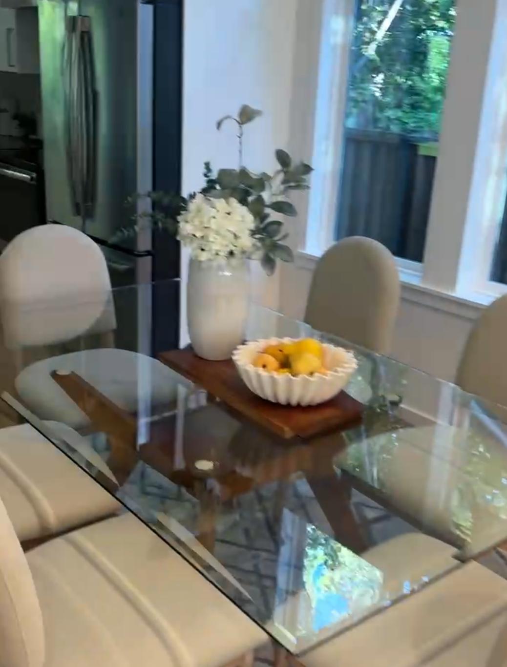 A staged dining table with chairs, flowers, and a bowl of fruit
